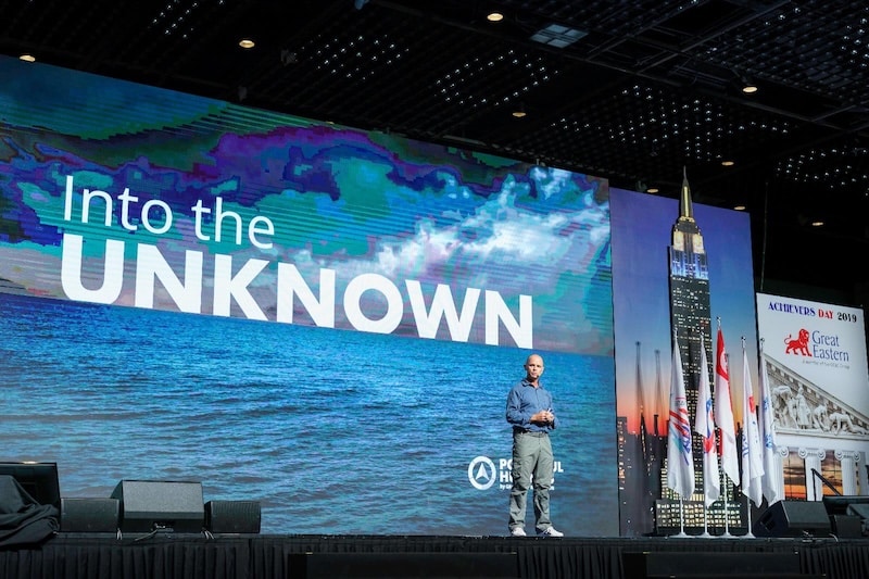 Explore Performance speaker presenting Into The Unknown on a large conference stage with ocean imagery.
